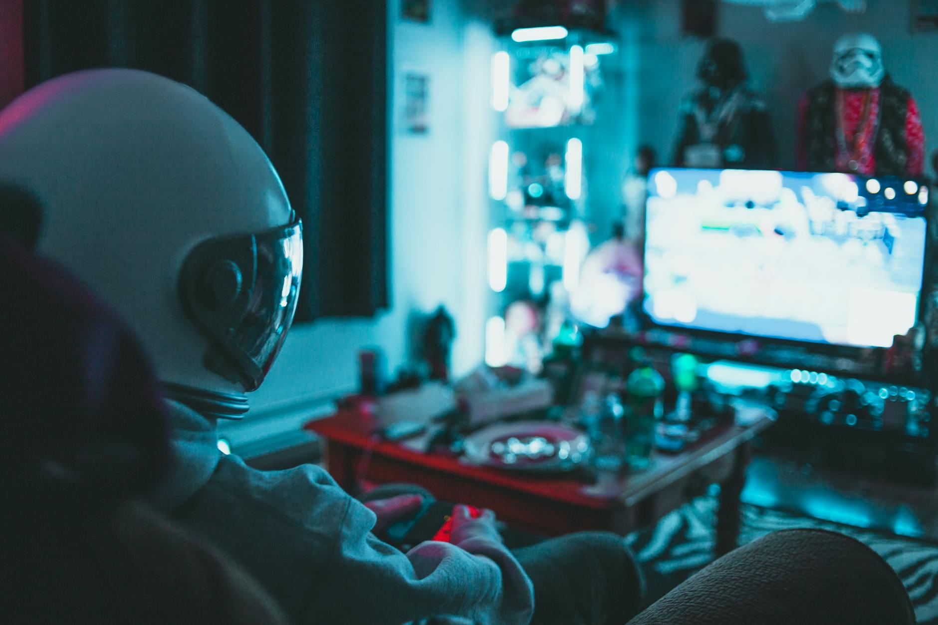 Osoba w goglach VR grająca padem na kanapie w ciemnym pokoju